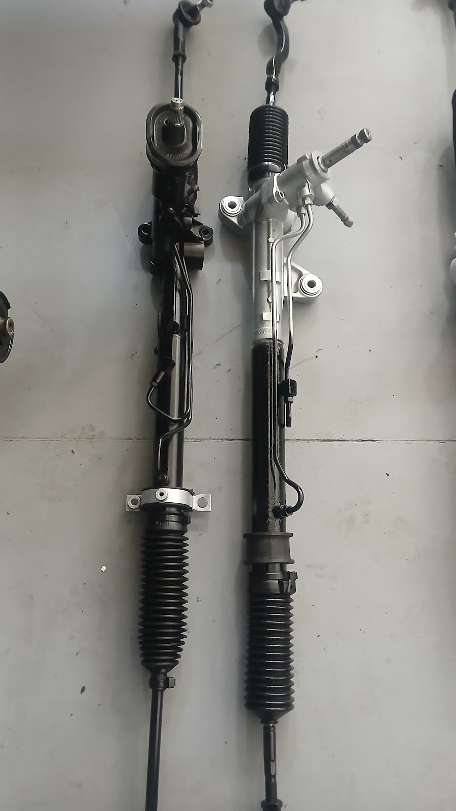 A worn steering rack next to a fully reconditioned steering rack, side by side